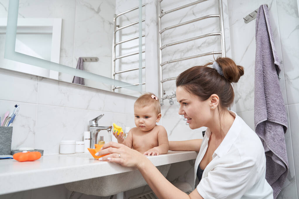 Niedliches kleines Kind sitzt im Waschbecken, während es drinnen mit Badespielzeug spielt - Foto, Bild