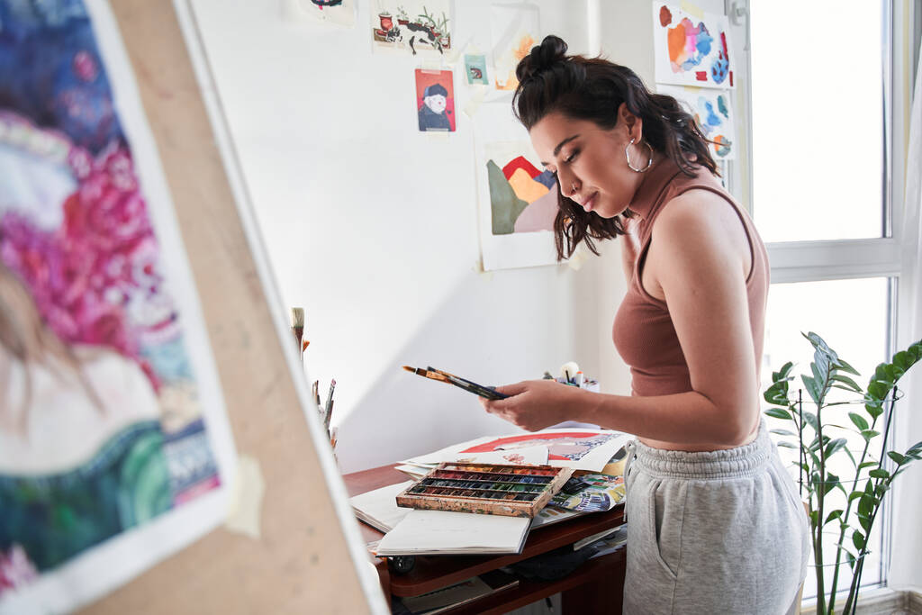 Γυναίκα καλλιτέχνης κοιτάζοντας τα πινέλα της με το πρόσωπο ευχαρίστηση, ενώ προετοιμασία για το σχέδιο στο σπίτι - Φωτογραφία, εικόνα