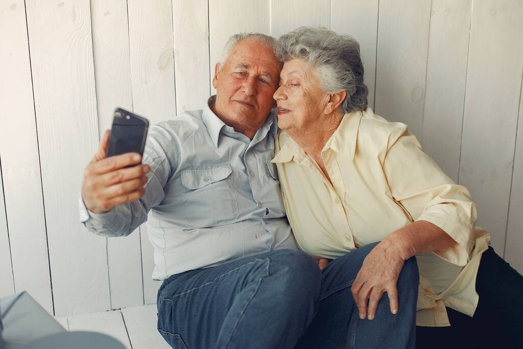 Elegant old couple sitting at home and using a phone - Photo, Image