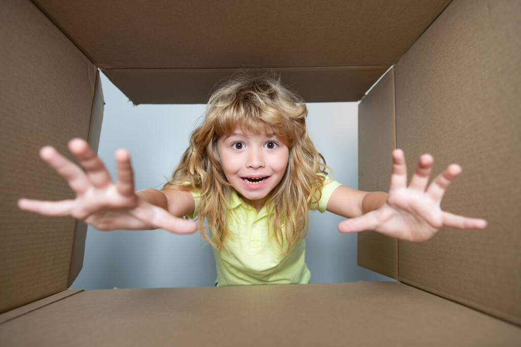 Счастливый ребенок с картонной коробкой, распаковывает посылку из интернет-магазина. Клиент доволен услугой быстрой доставки. Детское выражение удивленного лица. - Фото, изображение