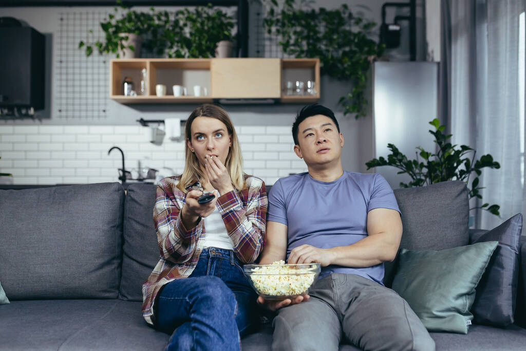 Couple man and woman at home watching TV together, bored switching channels, trying to find an interesting channel, family sitting on sofa at home - Photo, Image