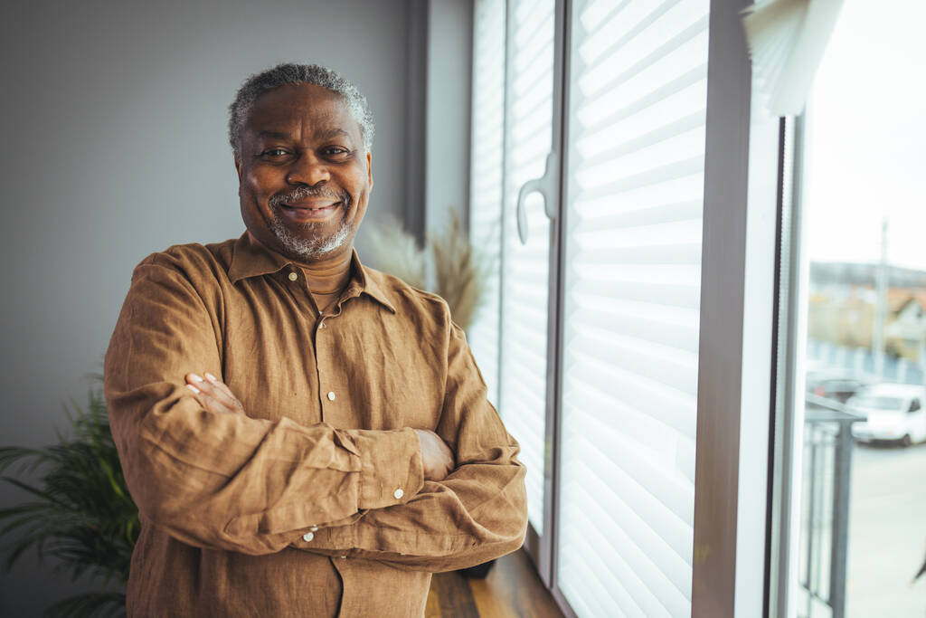 Afro-Amerikaanse Senior Man thuis Portret. Een lachende senior die naar de camera kijkt. Portret van een zwarte zelfverzekerde man thuis. Portret van een oudere man tegen een grijze achtergrond - Foto, afbeelding