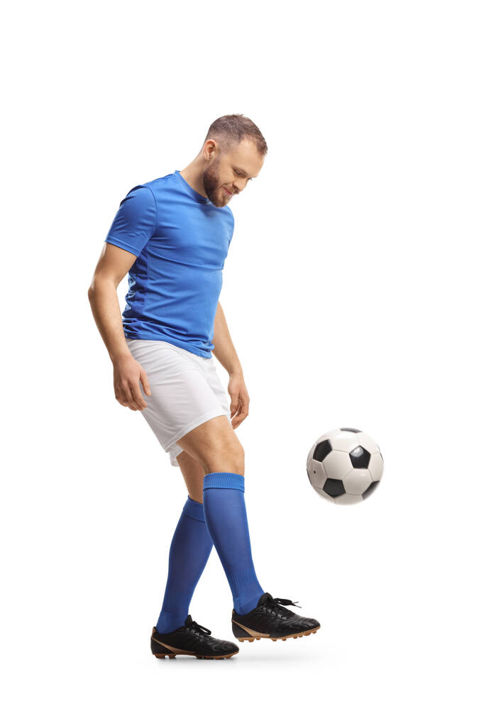 Largura completa de un futbolista en un top azul y pantalones cortos blancos pateando una pelota aislada sobre fondo blanco - Foto, Imagen
