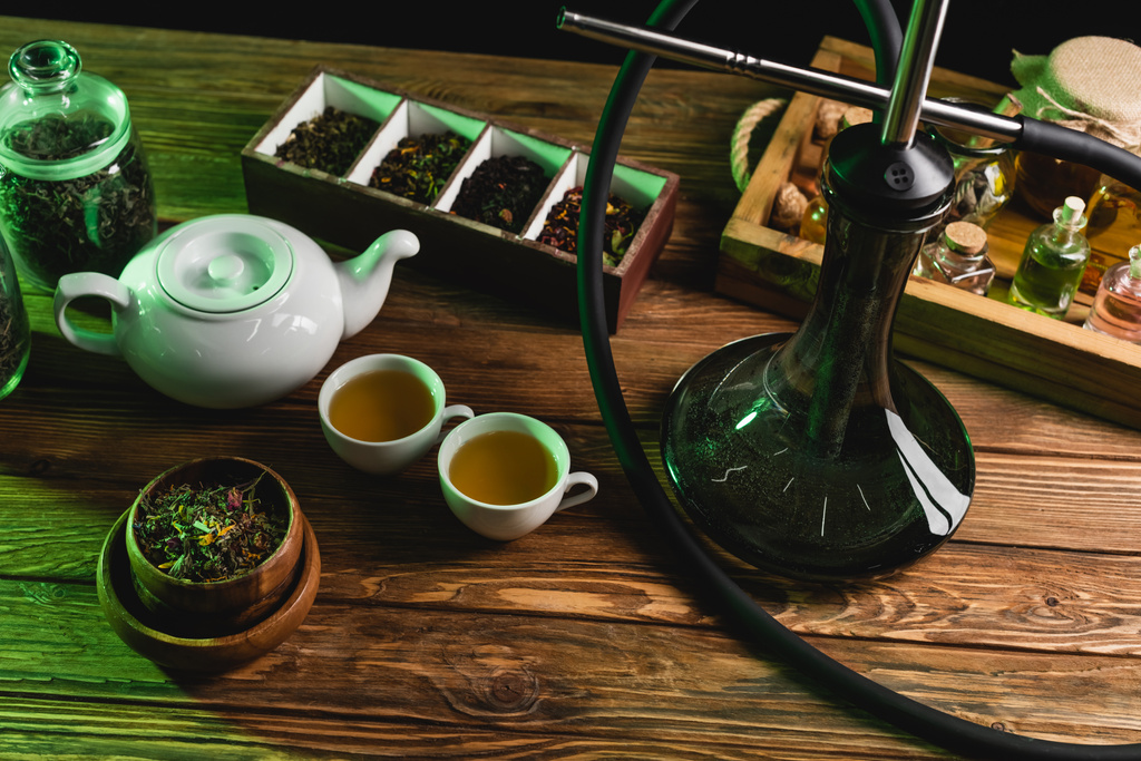 Top view of tea and hookah on wooden surface isolated on black  - Photo, Image