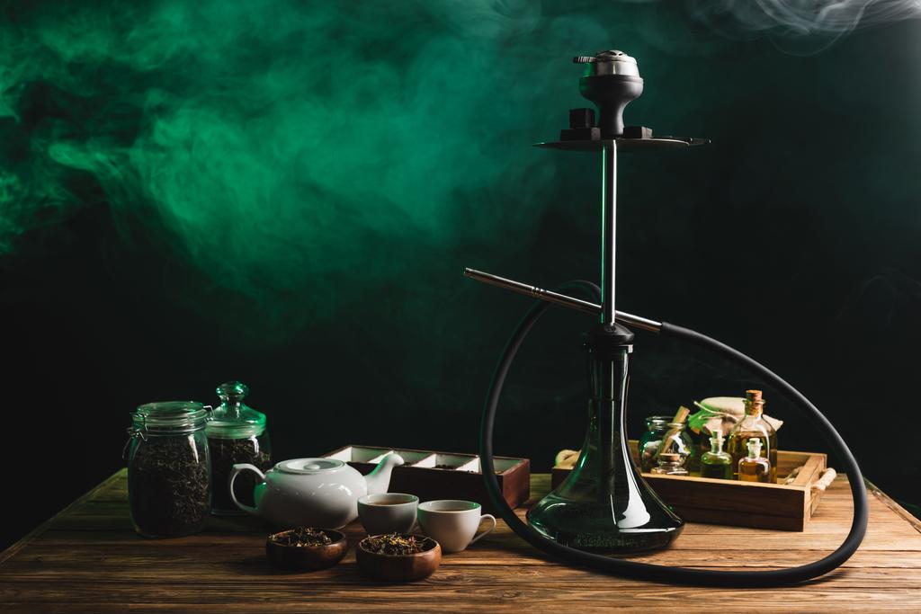 Thé et narguilé sur table en bois sur fond noir avec fumée - Photo, image