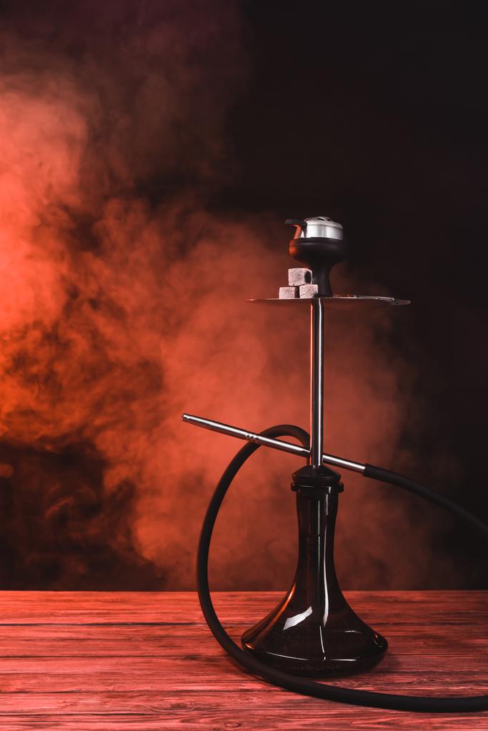 Hookah z węglem na drewnianej powierzchni na czarnym tle z czerwonym dymem  - Zdjęcie, obraz
