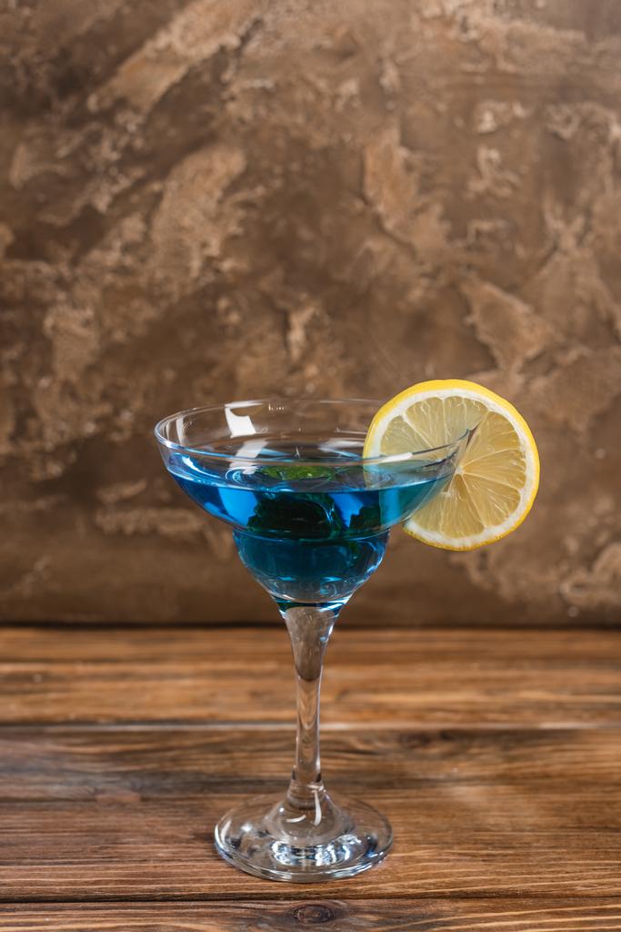 Синій коктейль у склі на дерев'яній поверхні на текстурованому кам'яному фоні
  - Фото, зображення