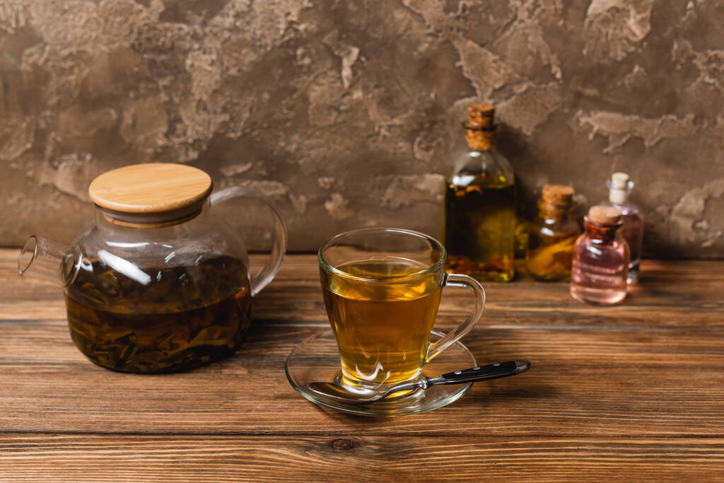 Çaydanlığın yanında bir fincan çay ve ahşap yüzeyde bulanık şişeler.  - Fotoğraf, Görsel