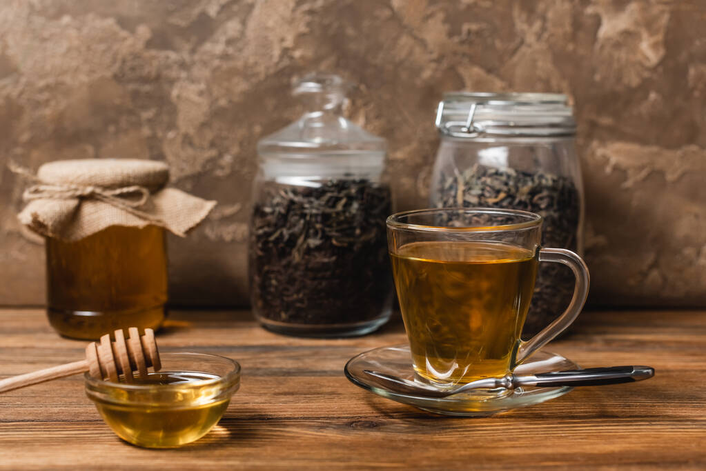 Kopje thee in de buurt van honing en wazig potten op houten oppervlak op textuur stenen achtergrond  - Foto, afbeelding