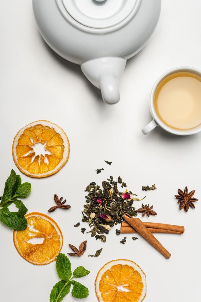 Bovenaanzicht van theepot bij droge thee, specerijen en munt op witte achtergrond  - Foto, afbeelding