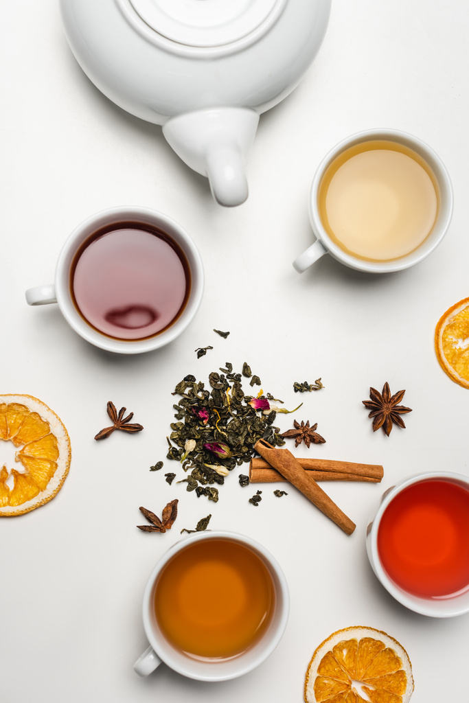 Top näkymä kuivia mausteita lähellä kuppeja teetä ja teekannu valkoisella pohjalla  - Valokuva, kuva
