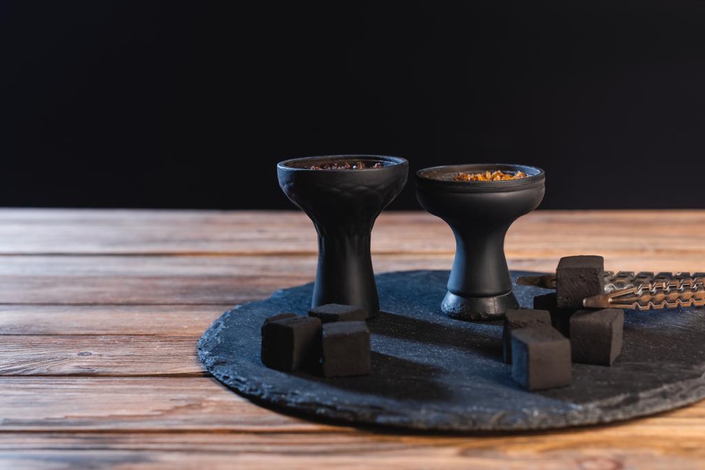 Charbons, pinces à épiler et bols de narguilé sur la surface en bois isolé sur noir  - Photo, image