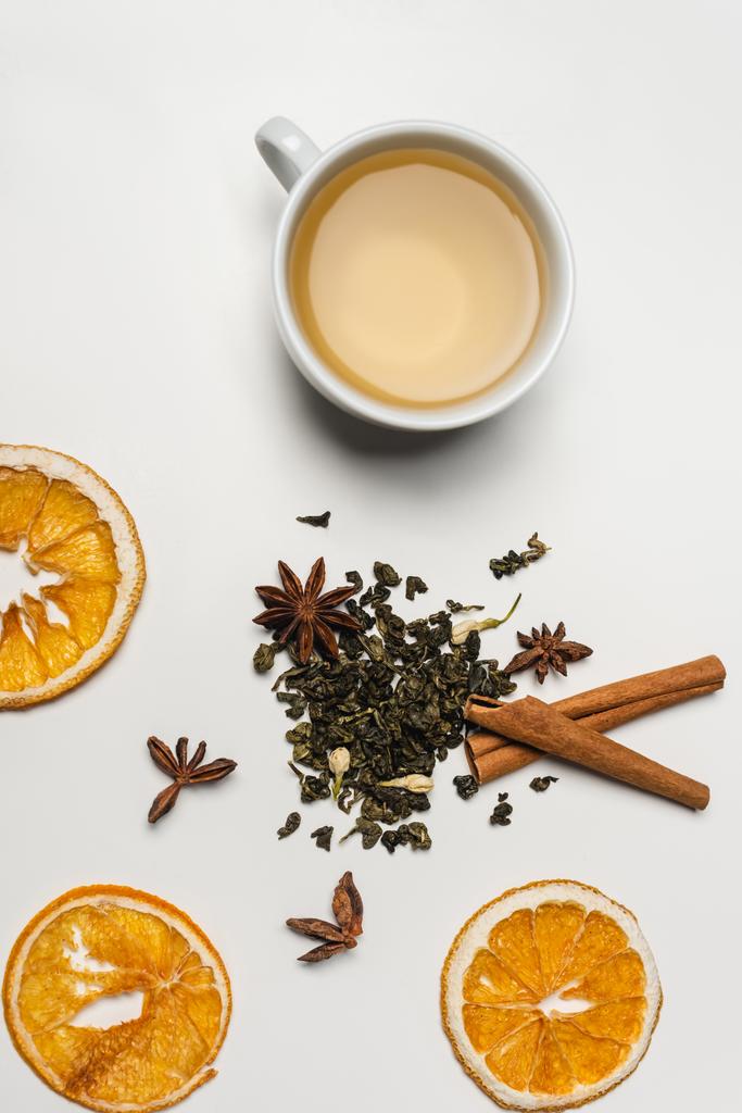 Vista superior de la taza de té cerca de especias secas y rodajas de naranja sobre fondo blanco  - Foto, imagen