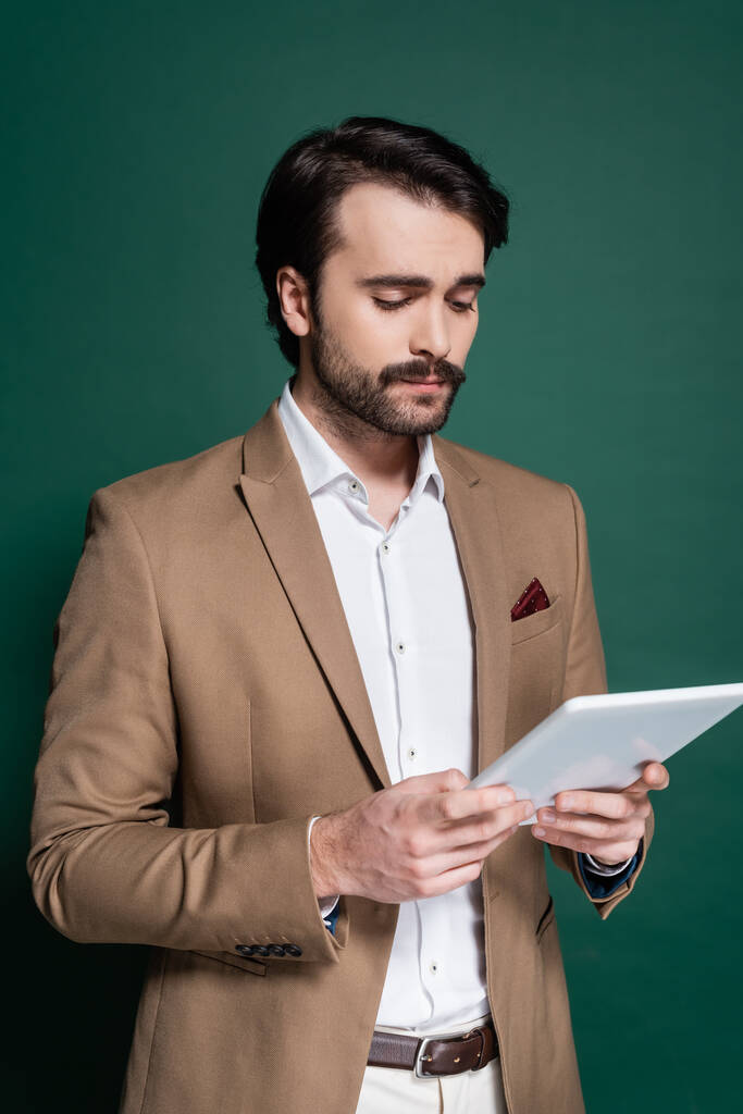 jeune homme avec moustache tenant tablette numérique sur vert foncé  - Photo, image