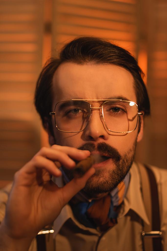 hombre en gafas fumando cigarro cerca de pantalla plegable borrosa - Foto, Imagen