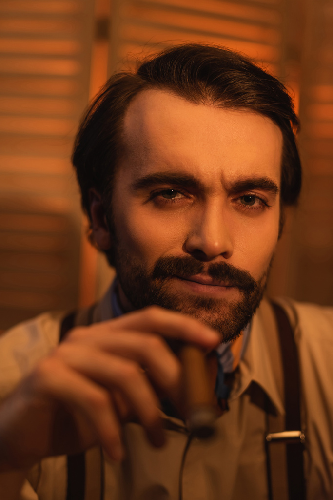 портрет человека с усами, держащего сигару и смотрящего в камеру на размытый складной экран - Фото, изображение
