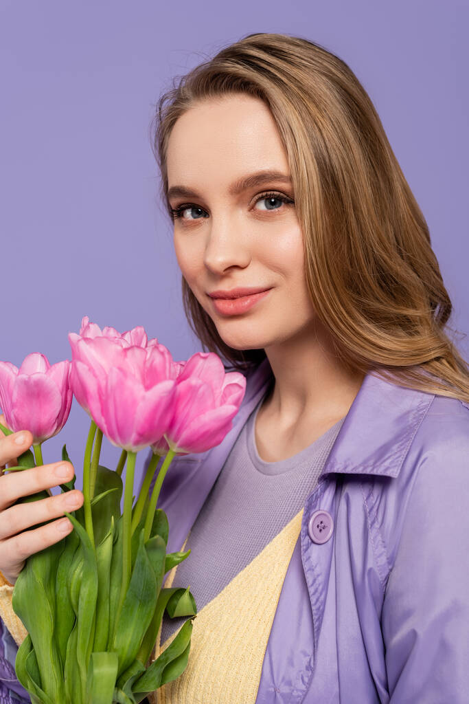 feliz joven sosteniendo tulipanes rosados aislados en púrpura - Foto, Imagen