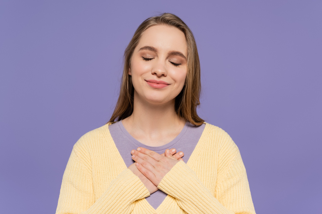 zufriedene junge Frau mit geschlossenen Augen, die Brust isoliert auf lila berührt - Foto, Bild