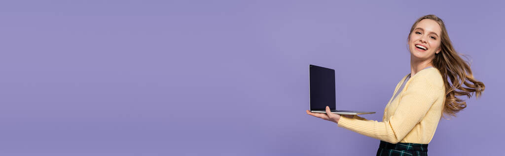 joyeuse jeune femme tenant ordinateur portable avec écran blanc isolé sur violet, bannière - Photo, image