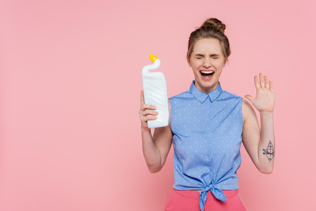 podekscytowana i wytatuowana młoda kobieta trzymająca butelkę z detergentem na różowo  - Zdjęcie, obraz