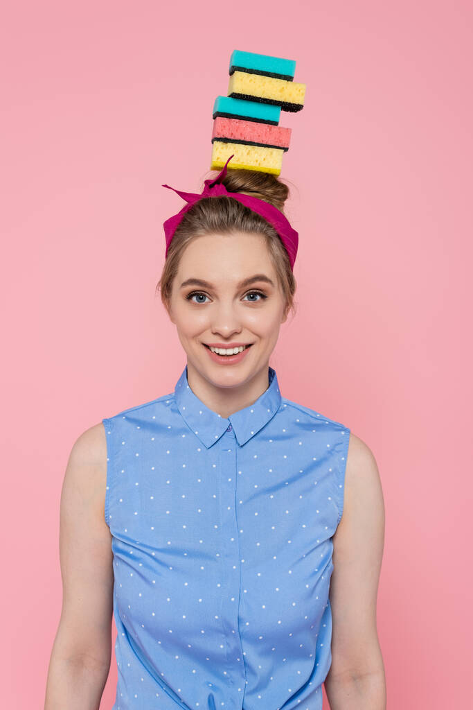 Ευτυχισμένη νεαρή γυναίκα με στοιβαγμένα σφουγγάρια στο κεφάλι απομονωμένα σε ροζ  - Φωτογραφία, εικόνα