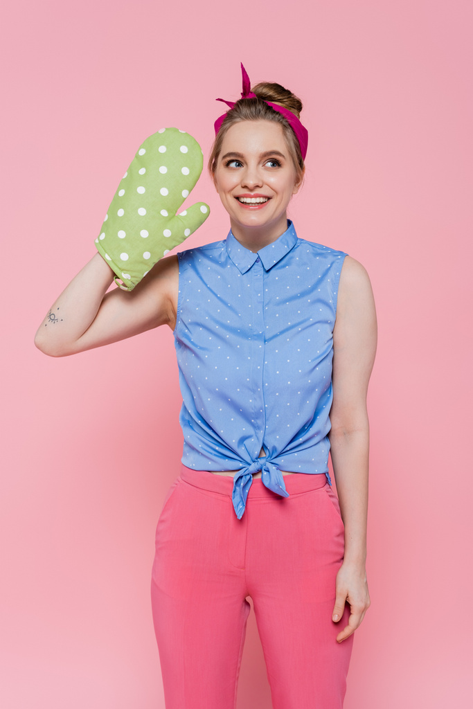 татуированная и счастливая молодая женщина в зеленой пекарской перчатке, изолированной на розовом - Фото, изображение