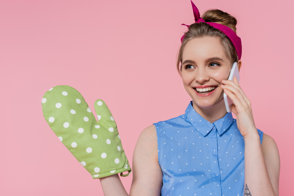 boldog fiatal nő zöld sütő kesztyű beszél okostelefon elszigetelt rózsaszín - Fotó, kép