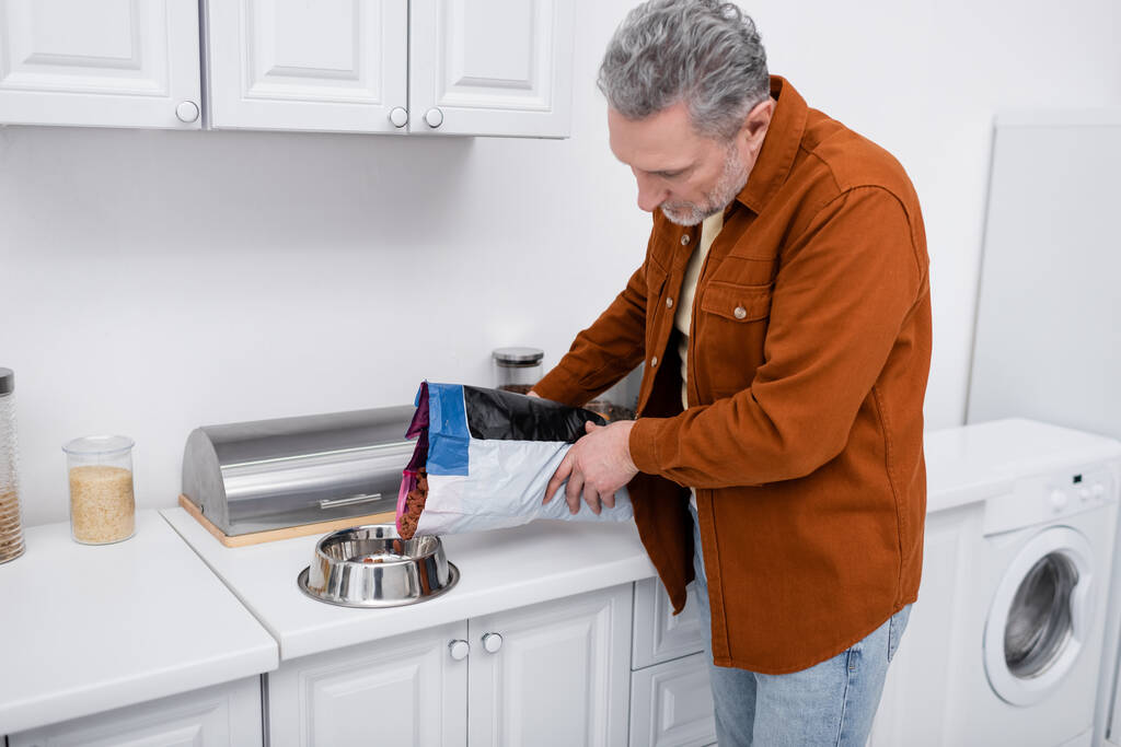 Kypsä mies kaatamalla koiran ruokaa kulhoon keittiössä  - Valokuva, kuva