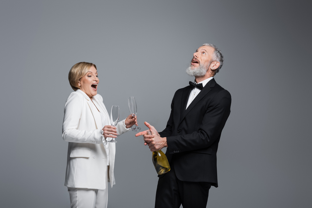 Eccitato maturo sposo apertura champagne vicino sposa con occhiali isolati su grigio  - Foto, immagini