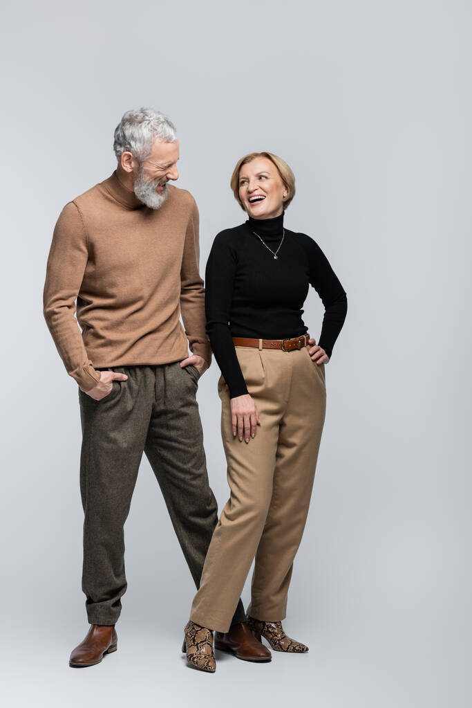Cheerful stylish woman looking at mature husband on grey background  - Photo, Image