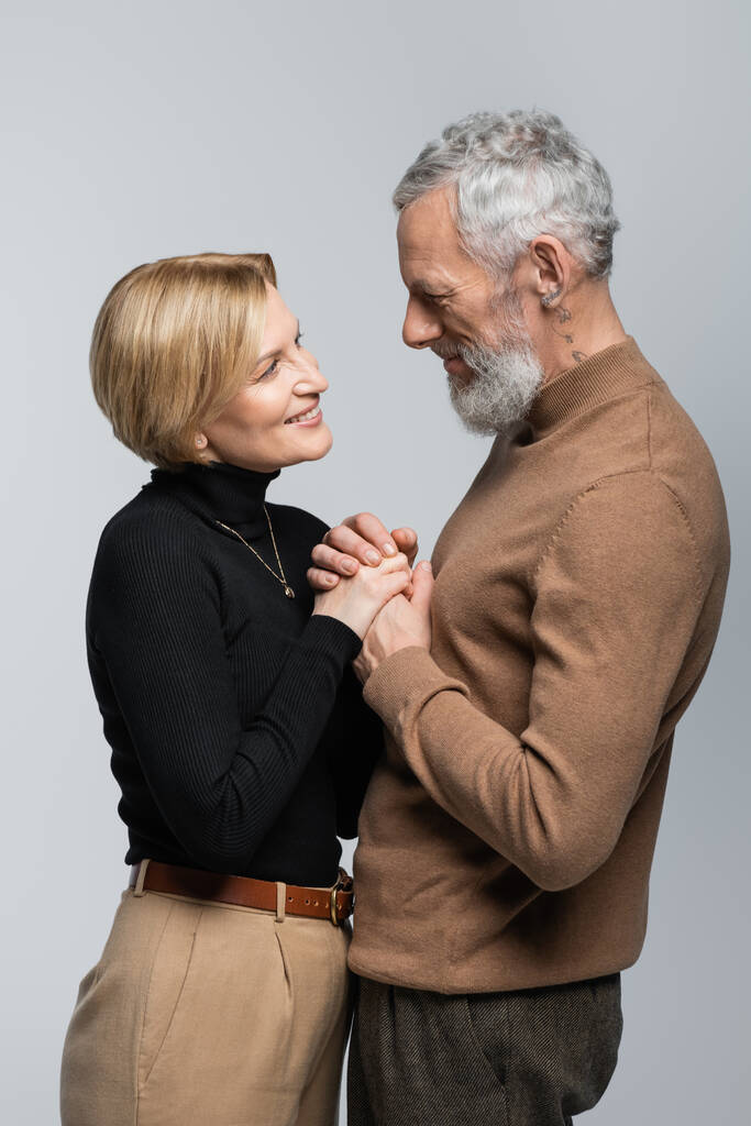Joyeux couple mature et élégant tenant les mains isolées sur gris  - Photo, image