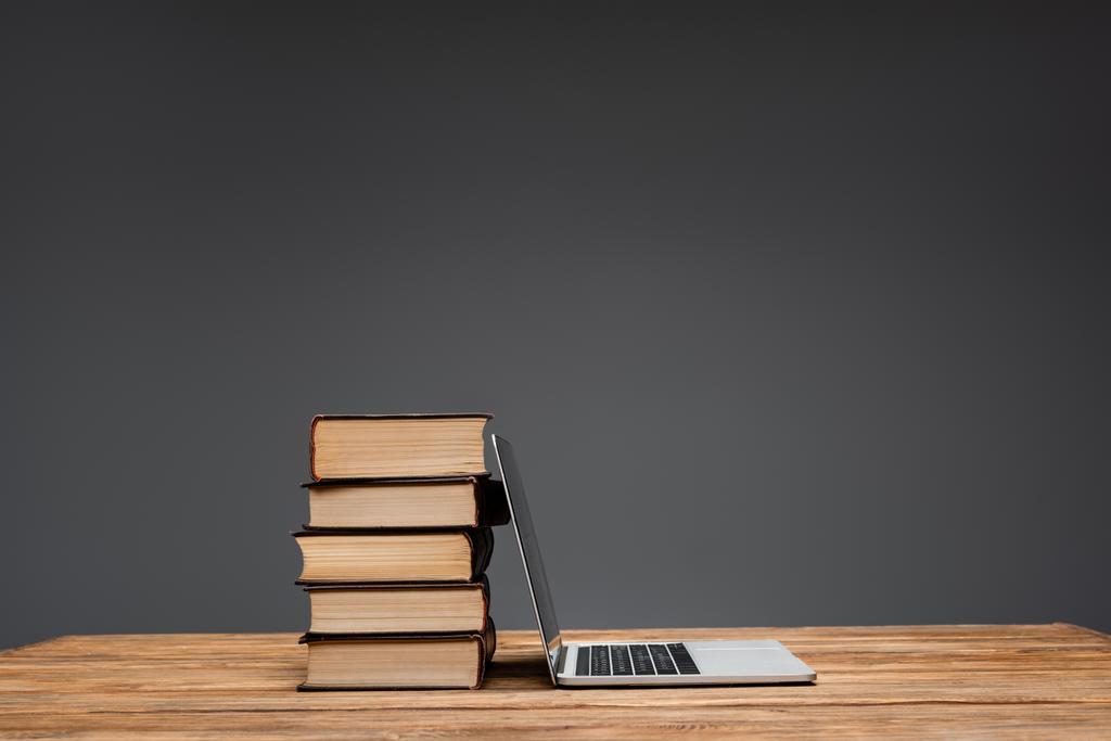 pile of books and laptop on brown wooden surface isolated on grey - Photo, Image
