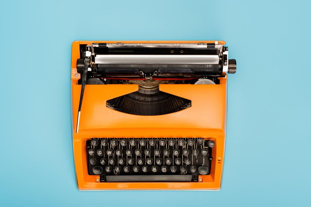 top view of orange typewriter with black keyboard isolated on blue - Photo, Image