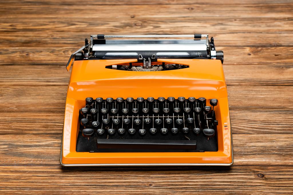 leuchtend orange Schreibmaschine mit schwarzer Tastatur auf strukturierter Holzoberfläche - Foto, Bild
