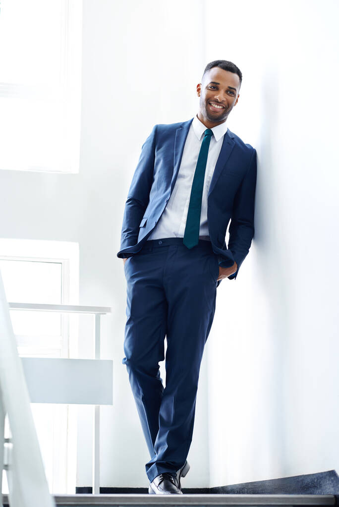Il a l'air élégant dans sa tenue de travail. Un bel homme d'affaires afro-américain appuyé contre un mur à l'intérieur. - Photo, image