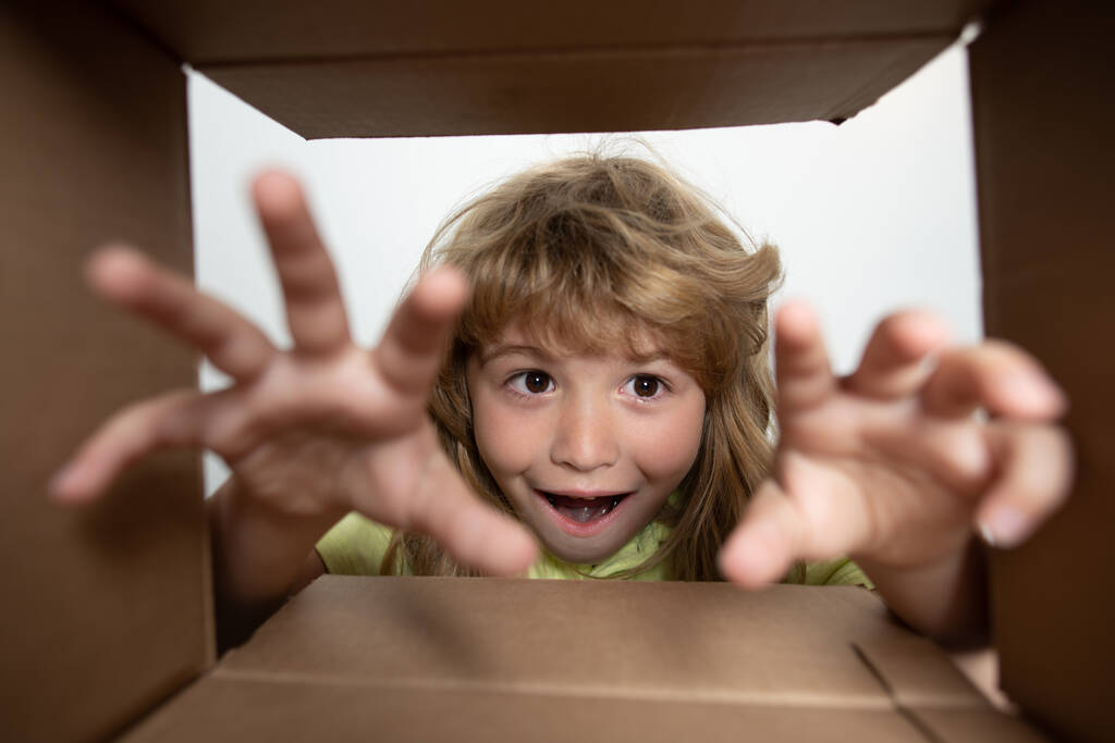 Grappig opgewonden kind dat de kartonnen doos uitpakt en opent terwijl hij erin kijkt. De kleine kinderen unboxing geschenk in het zicht. Kind jongen kijken verrast in een geschenk. - Foto, afbeelding
