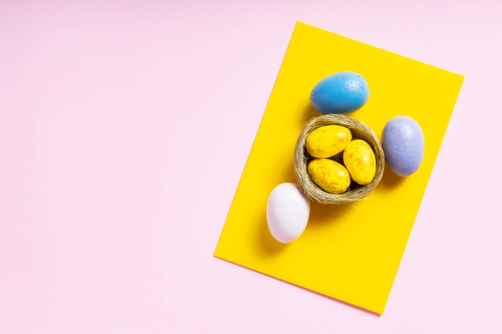 Huevos de Pascua multicolores sobre un fondo rosa. Huevos pintados en un nido natural. Feliz concepto de Pascua. Vista superior. Copiar espacio - Foto, imagen