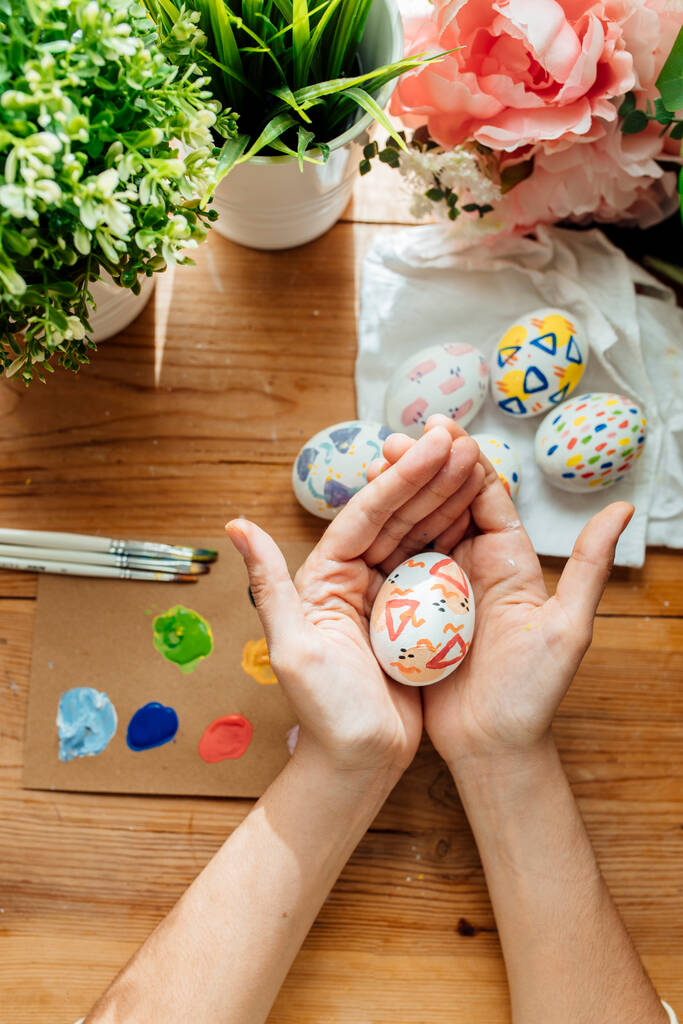 Donna con in mano un uovo di Pasqua moderno. Spazzole e vernici con fiori e piante. Felice concetto pasquale su uno sfondo di legno. - Foto, immagini