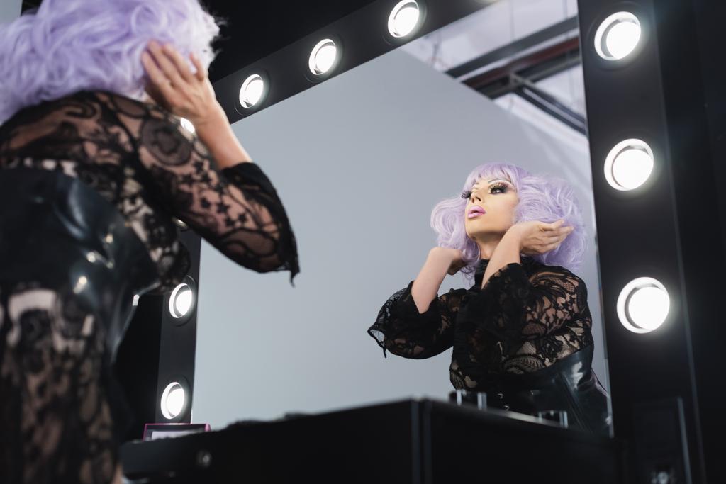 Niedrige Blickwinkel der Glamour Drag Queen Einstellung violette Perücke in der Nähe von Spiegel - Foto, Bild