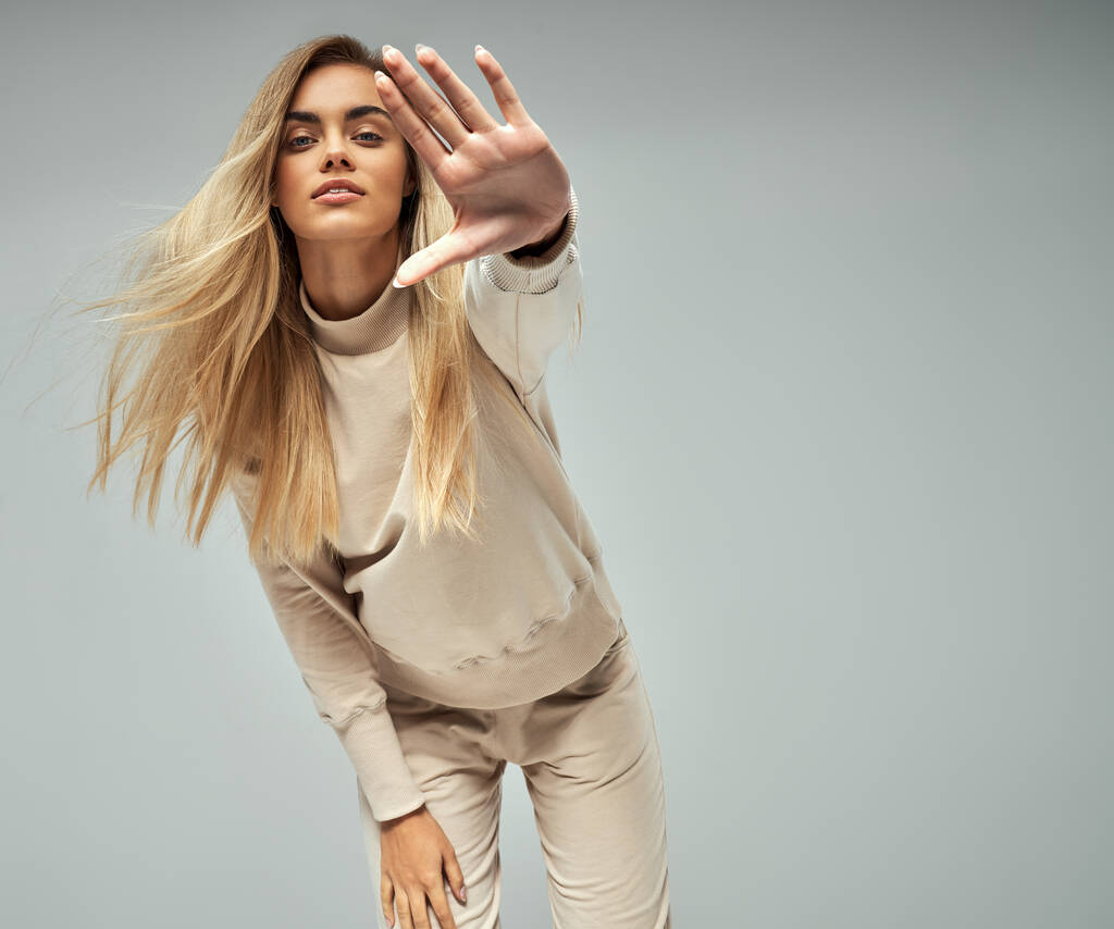 Blonde woman wear of beige set of tracksuit showing stop gesture isolated on grey background - Photo, Image