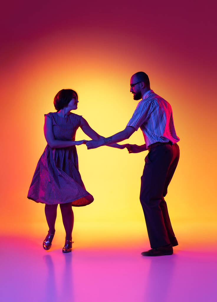 Retrato de homem e mulher animado, casal de dançarinos em roupas vintage estilo retro dançando dança lindy hop isolado no gradiente amarelo e roxo fundo. - Foto, Imagem