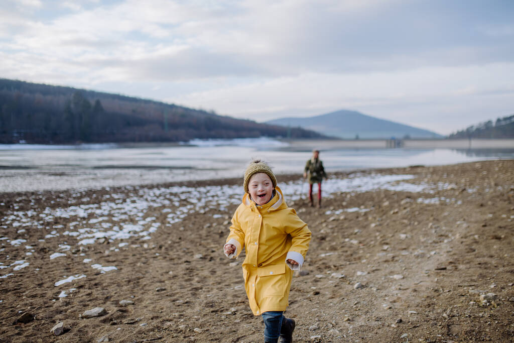 Szczęśliwy chłopczyk z Downem biegający zimą nad jeziorem.. - Zdjęcie, obraz