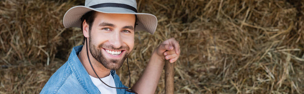 nuori maanviljelijä lierihattu hymyillen kameralle lähellä heinäsuova, banneri - Valokuva, kuva