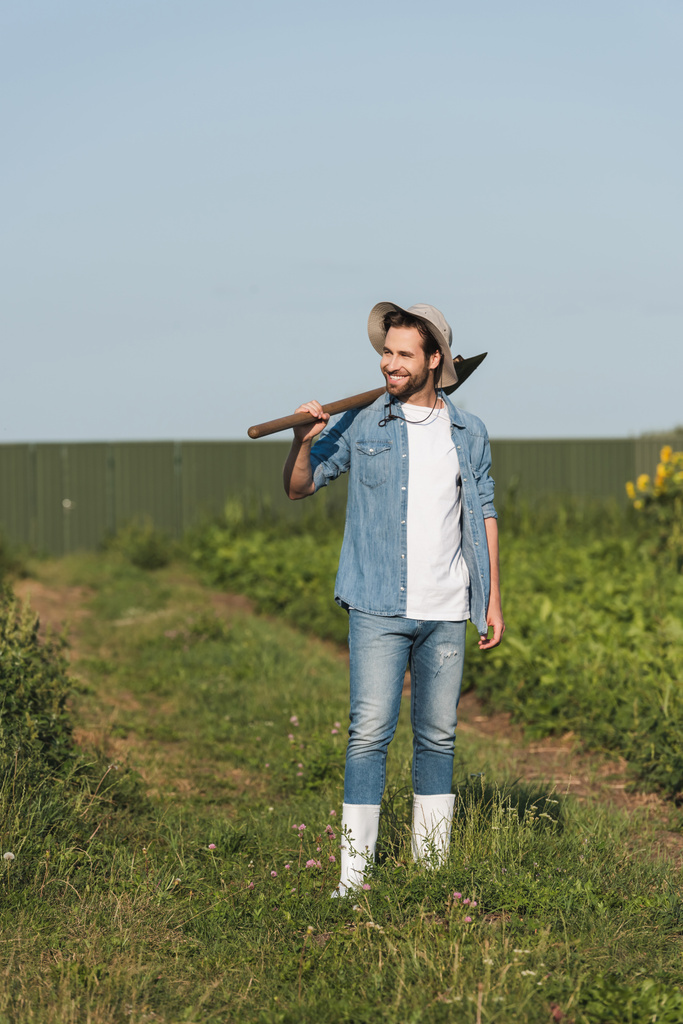 visão de comprimento total do jovem agricultor com pá sorrindo no campo - Foto, Imagem