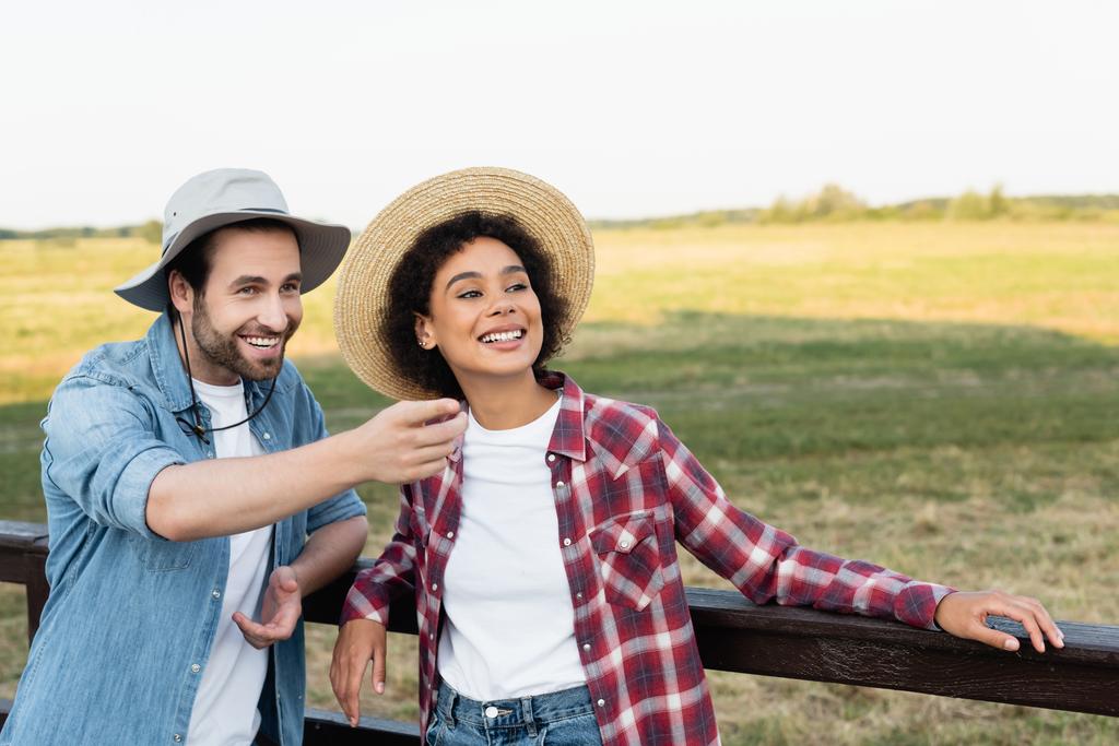farmer looking away and pointing with finger near happy african american colleague - Photo, Image