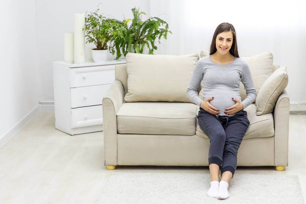 Foto de una mujer embarazada mirando a la cámara y tocándose el estómago. - Foto, Imagen