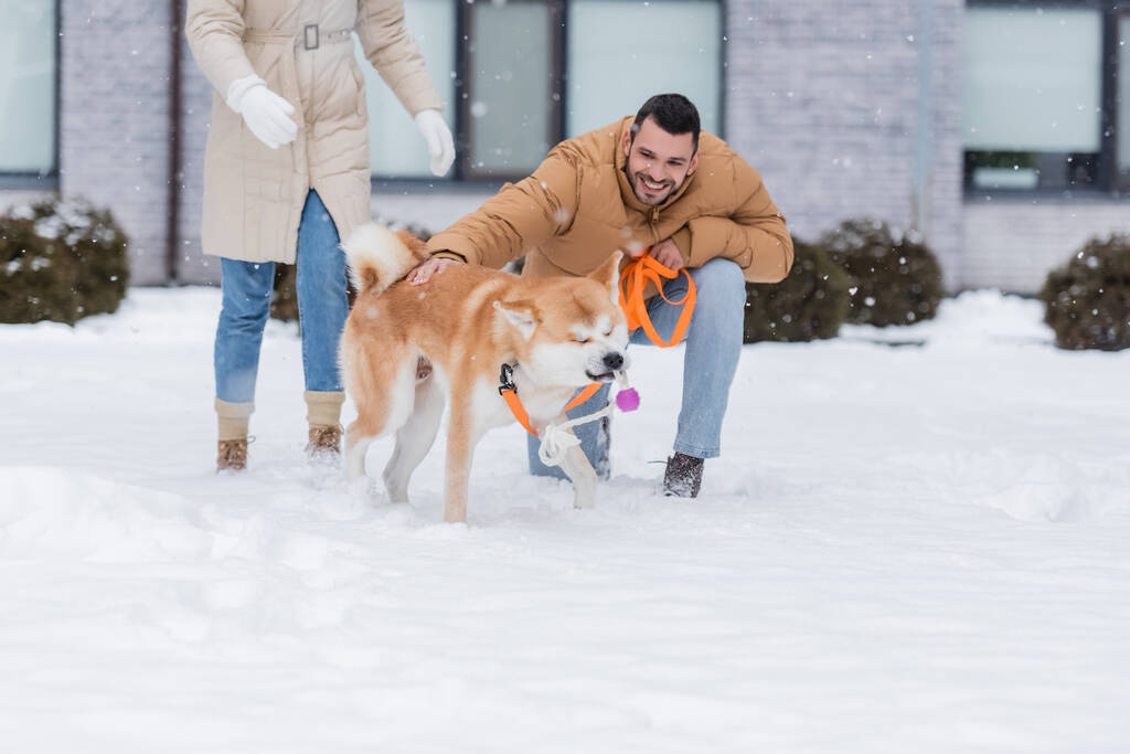 happy man holding leash while petting akita inu dog near girlfriend outside - Photo, Image