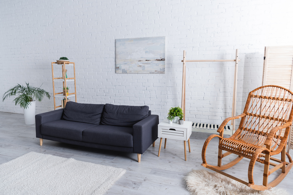 moderna sala de estar con sofá, plantas verdes y mecedora de ratán  - Foto, imagen