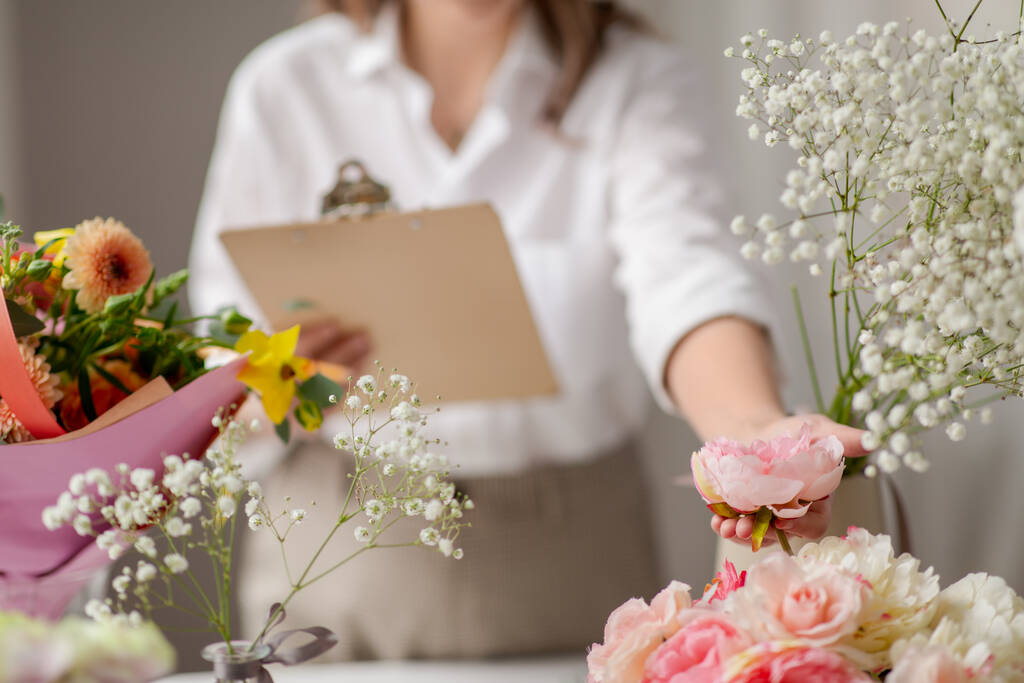 mulher feliz com prancheta e flores no estúdio - Foto, Imagem