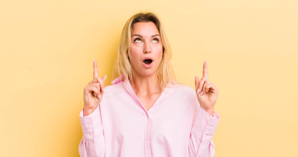 blonde caucasian woman feeling awed and open mouthed pointing upwards with a shocked and surprised look - Photo, Image